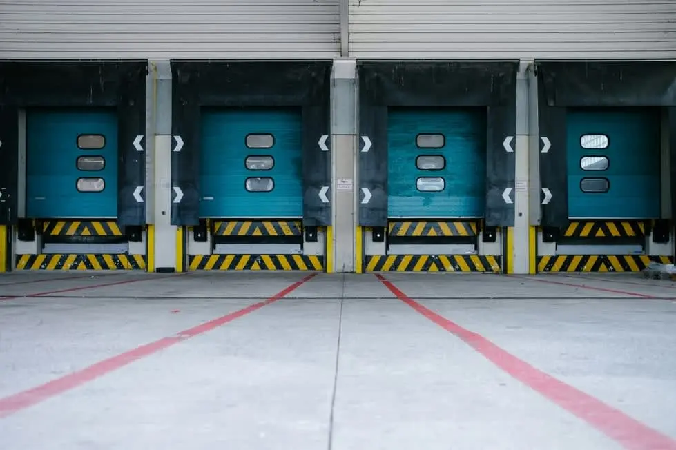 Row of blue loading dock doors with yellow safety markings at a warehouse