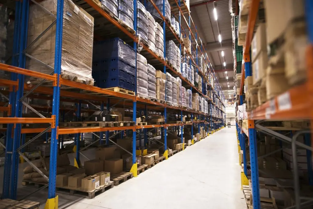 Spacious warehouse aisle with orange and blue shelving units stocked with pallets and boxes